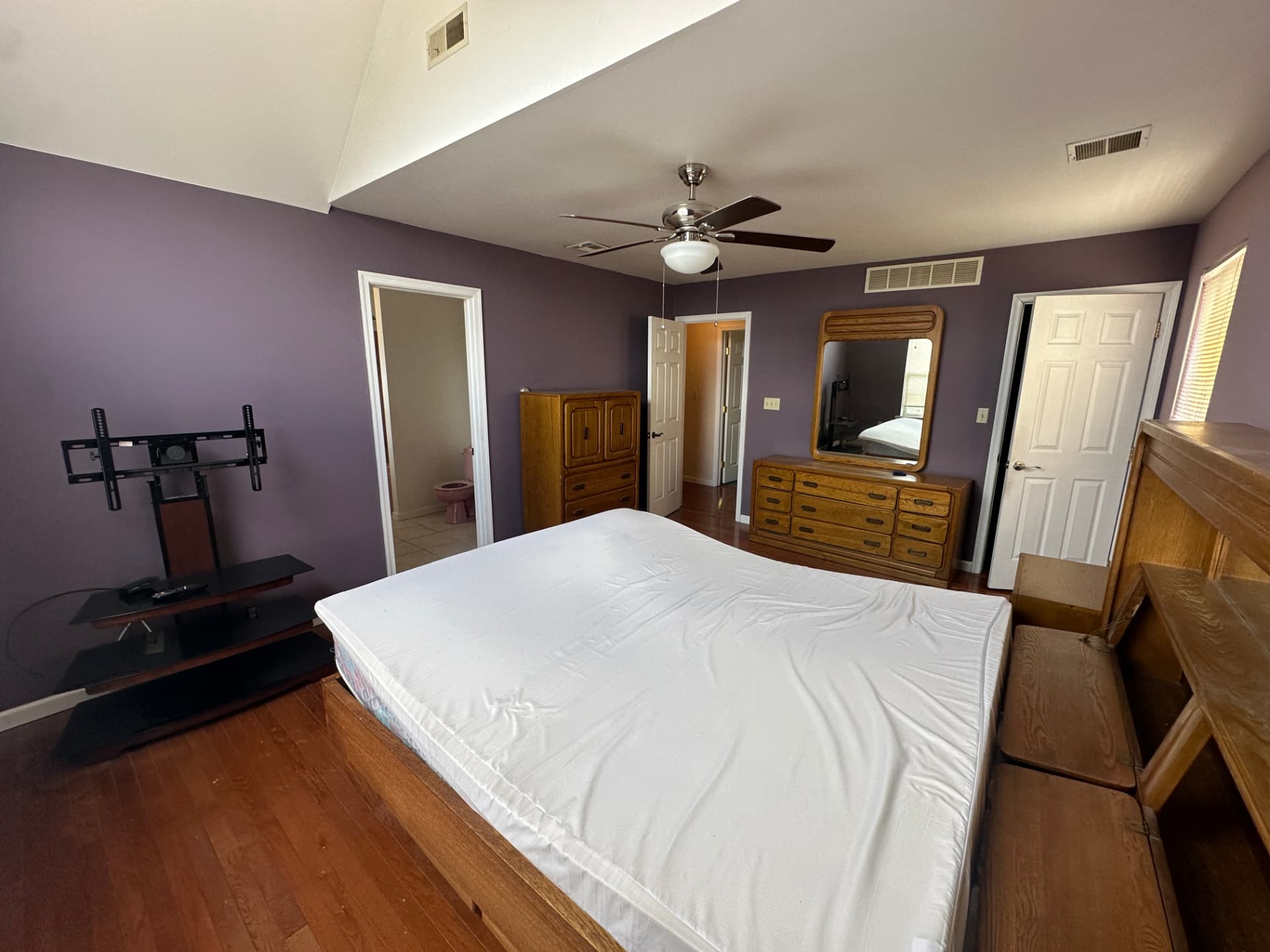 Bedroom with hardwood flooring, vaulted ceiling, and an attached bathroom